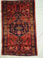 Full view of rug laid flat showing red field with central navy medallion and geometric motifs bordered by a patterned frame.