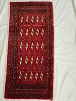 Full view of a small rectangular Turkman rug with geometric medallion pattern on deep red background and detailed borders