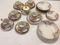 Full set laid out showing cups, saucers, plates, sugar bowl, and creamer with consistent hand-painted and gilded Art Deco floral designs.