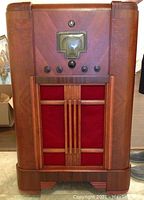 Full front view of large antique wooden tube radio cabinet with tuning dial and multiple control knobs.