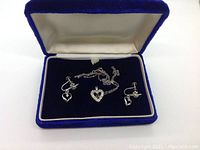Blue velvet jewelry box open showing both heart-shaped pendant necklace and matching screw-back earrings on black interior