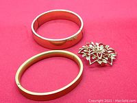Photo of two gold filled bracelets and one floral brooch on red background showing overall lot.
