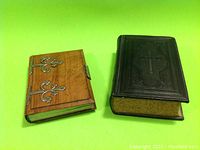 Both books side by side, showing black leather German Bible and smaller olive wood bound handwritten poetry book with metal clasps.