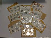 Nine sealed uncirculated Canadian coin sets in beige envelopes and one loose 1967 silver dollar on a table.