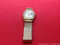 Gold-tone Rotary wristwatch with cushion-shaped case and linked bracelet laid on red background, showing face and band details.