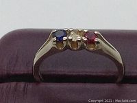 Close-up photo of the 10K gold ring showing three colored stones: blue, clear, red, and part of the ring band.