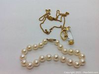 Photo showing the pearl bracelet with round white pearls and a 14K gold clasp alongside the Swarovski crystal golf bag pendant necklace with a gold-tone chain.