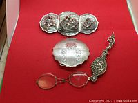 All three items arranged on red background: lorgnette, buckle, compact