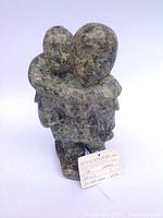 Front angled view of the sculpture showing the embracing mother and child figures with attached authenticity tag.