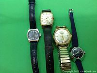 Four watches laid flat on a green background, showing front dials and straps.