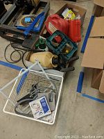 Top-down photo showing multiple boxes containing power tools, sprayer, and various hardware supplies on a concrete floor.
