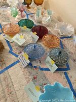 Set of seven vintage glass candy dishes in Federal Glass Windsor Button & Cane pattern with lids on quilted surface.