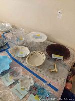 Photo showing assortment of vintage glass and ceramic serving bowls and plates on a patterned cloth surface with tags.