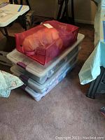 Three stacked large plastic storage bins visible, top bin with orange yarn inside, bins have purple latches