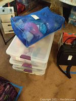Blue mesh bag with assorted yarn skeins on top of three clear plastic storage bins containing additional yarn