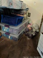 Plastic containers and bags containing yarn spools and skeins in assorted colors stored under a bed.