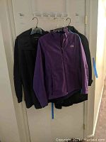 Three jackets hanging on a door: black (Athleta and London Fog), purple The North Face jacket in front