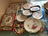 Several decorative plates arranged on a table, showing a variety of floral designs and styles including scalloped edges and detailed painting.