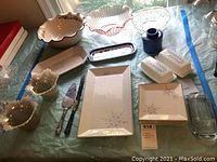 Photo of assorted serving bowls, butter dishes, butter crock, serving tray with plates, cake cutters and candle holders arranged on a table.