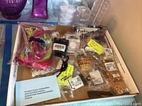 Box containing a variety of rhodium alphabet charms in small clear plastic containers, assorted silver tone chains and gold tone chain segments with clasps in plastic bags.