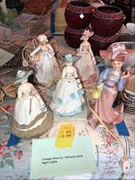 Photo of five vintage female porcelain night lights with floral and period costumes, showing cords and tags