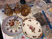 Full view of glass figurines, plates, compotes, and vases on quilted cloth showing detailed textures and iridescent finishes.
