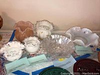 Photo of seven Fenton glass bowls and vases with ruffled edges and iridescent finishes laid on a table.