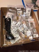 Box containing multiple small plastic bags with assorted jewelry findings including bead side clasps, clasps with vertical loops, gold plated earring hooks, sterling silver hooks, and other components.