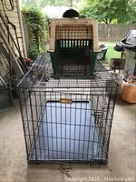Photo showing smaller plastic pet crate with metal wire door on top of larger black metal wire pet crate with plastic tray base