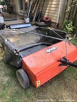 Photo of Agri-Fab lawn sweeper angled view showing metal sweep housing and black mesh collection bag attached.