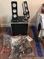 Photo of Logitech Z4 speakers with wired satellite speakers placed on top of the subwoofer. Plastic bag with trail camera and accessories in front, and partially visible card game box to the right.