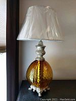 Amber globe lamp with ornate silver metal details and white lampshade still in protective plastic.