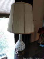 Full view of vintage table lamp by window with natural light showing glass base with floral design and beige fabric shade