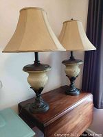 Pair of Kathy Ireland table lamps with beige fabric bell-shaped shades and textured cream-colored glass bases with metal detailing, placed on a wooden surface