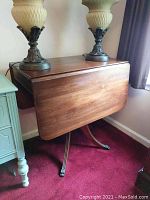 Photo of vintage drop leaf wood table with lamps on top, showing side and top view with one leaf down.