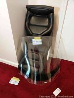 Wide view showing black leather seat with headrest behind the tinted windshield on a red carpet.