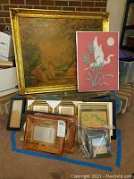 Full view of large framed classical garden scene painting alongside framed fabric bird art and multiple smaller frames stacked.
