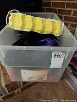 Transparent storage bin with several workout equipment pieces inside and yellow elastic bands in a mesh pouch on top.