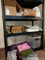 Black shelf holding several flat packed brown cardboard box shapes, some plastic bags, and folded tissue paper.