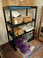 Full view of a black plastic shelving unit containing various stored items including boxes, bags, and bins on different shelves.