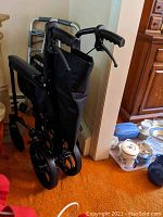 Folded aluminum transport wheelchair with black seat and back, showing rear wheels and handles.
