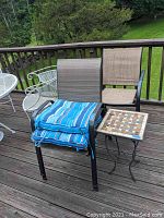 Four stackable outdoor patio chairs with brown mesh fabric seating and backs, two blue striped seat cushions stacked on one chair, and a small square decorative tile top table on a wooden deck.