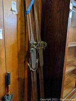 Pair of vintage wooden skis with leather strap bindings hanging on wall.