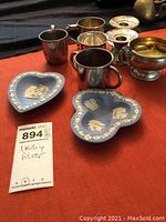 Photo showing sterling silver cups, weighted candle holders, and two Wedgwood dishes on a red surface.