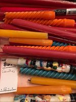 Multiple twisted taper candles in various colors and a Christmas-themed taper candle with snowman design mixed in with damask napkins underneath