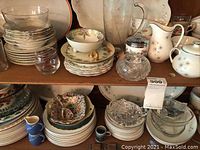 Shelves displaying assorted china including Royal Doulton Thistledon bowls, cups, plates, Nippon hand painted pieces and clear glass serving bowls.