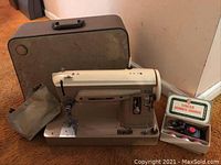 Singer vintage sewing machine with attached pedal, carrying case and box with accessories placed on carpeted floor