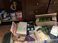 Photo of various unopened personal hygiene medical supplies including wipes, bandages and dressings arranged on floor in front of wooden cabinetry.