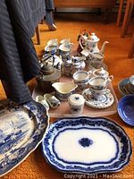 Full view of assorted blue and white porcelain tableware including teapots, teacups, creamers, jam jars, and platters on orange carpet