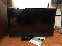 Front view of the Panasonic Viera 32 inch LCD HDTV with remote control and owner's manual placed in front of the TV.